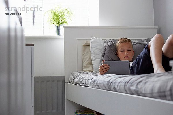 Blick durch die Tür des auf dem Bett liegenden Jungen mit Blick auf das digitale Tablett