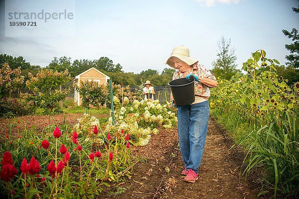 Seniorin beim Blumen gießen mit Eimer auf dem Bauernhof