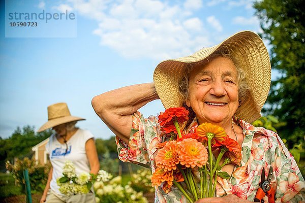 Seniorin mit Strohhut und Blumen auf dem Bauernhof