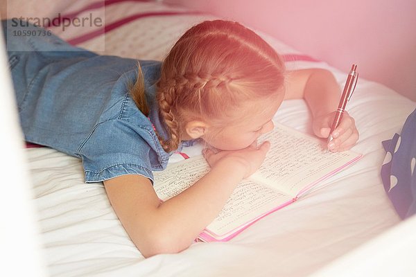 Hochwinkelansicht des auf dem Bett liegenden Mädchens in einem Notizbuch