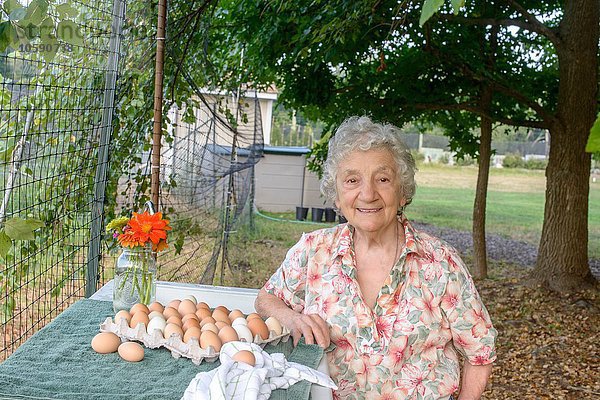 Seniorin posiert neben einem Tablett mit Eiern auf dem Bauernhof