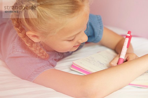 Beschnittene Ansicht des Mädchens auf dem Bett Schreiben im Notizbuch