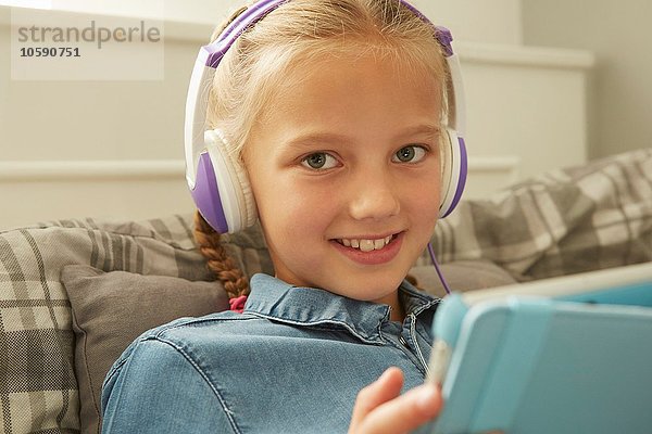 Mädchen mit Kopfhörern  die ein digitales Tablett halten und lächelnd auf die Kamera schauen.