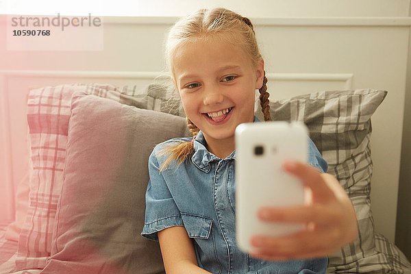 Mädchen sitzt auf dem Bett mit dem Smartphone zu nehmen Selfie lächeln