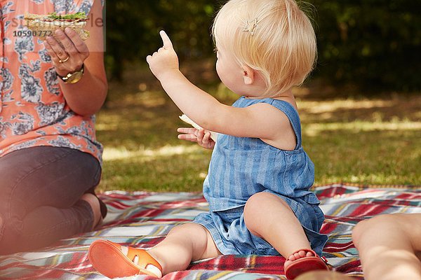 Frau und kleines Mädchen sitzen auf einer Picknickdecke und picknicken.