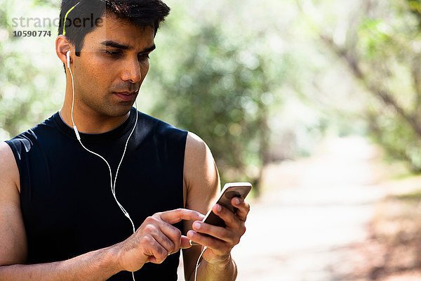 Jogger beim Auswählen von Musik auf dem Smartphone im Park