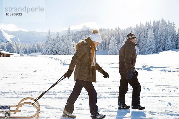 Seitenansicht des Seniorenpaares auf schneebedecktem Schlitten  Sattelbergalm  Tirol  Österreich