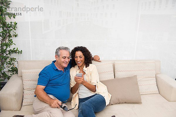 Senior Mann und Frau lesen Smartphone-Texte auf der Terrasse Sofa