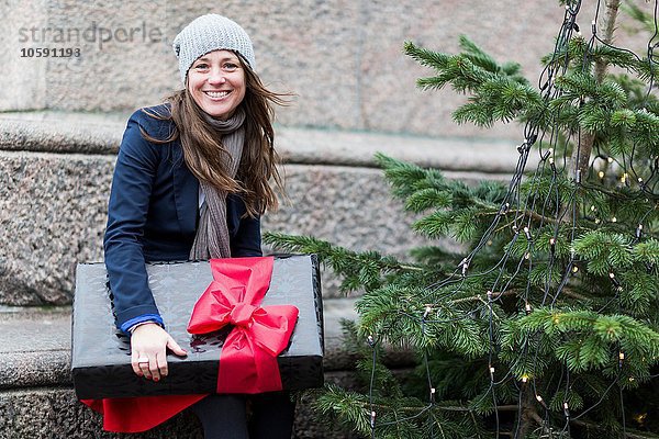 Portrait der reifen Frau mit Weihnachtsgeschenk neben dem Weihnachtsbaum