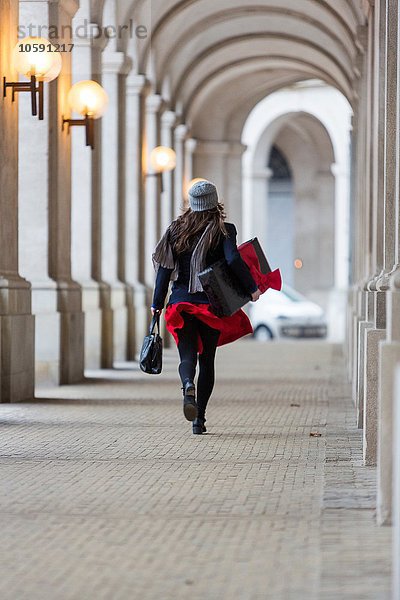 Rückansicht der reifen Frau mit Weihnachtsgeschenk beim Spaziergang durch die Stadtkolonnade