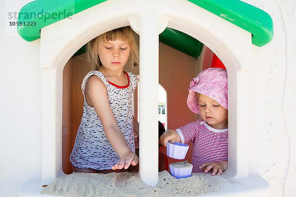 Kleinkind und Schwester spielen mit Sand auf einer Fensterbank