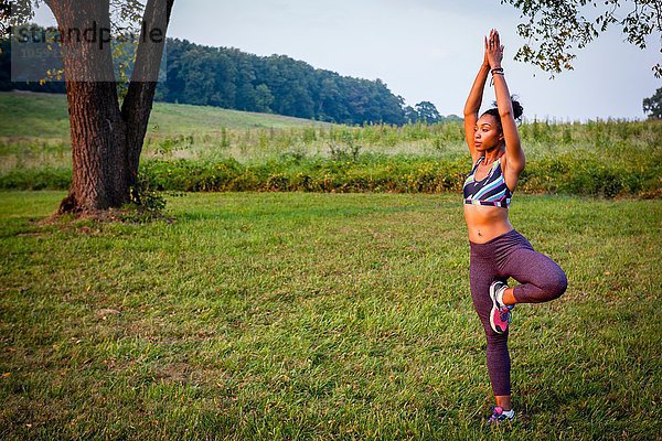 Junge Frau praktiziert Yogabaum-Pose im ländlichen Park