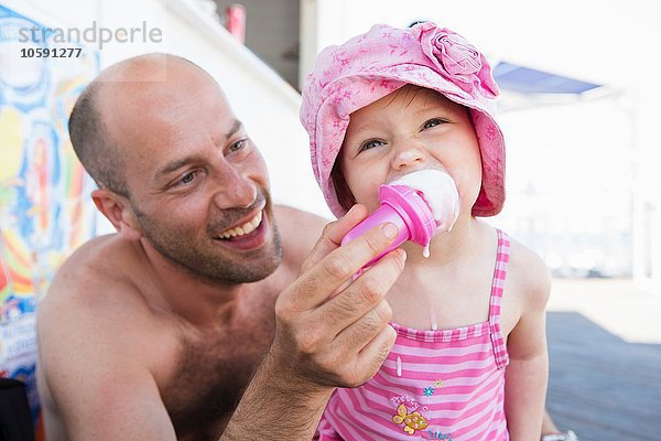 Vater füttert Kleinkind Tochter Eistüte am Strand