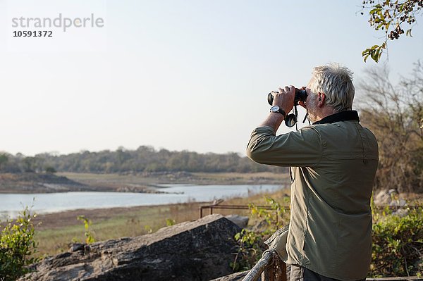 Älterer Mann  der durch ein Fernglas auf den Fluss schaut  Kafue Nationalpark  Sambia