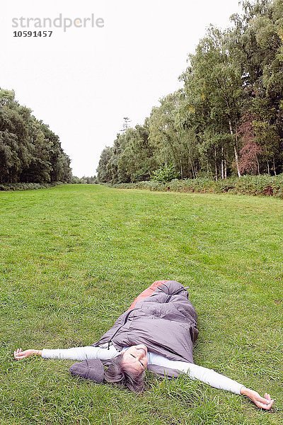 Seniorin im Schlafsack  im Feld  Arme ausgestreckt