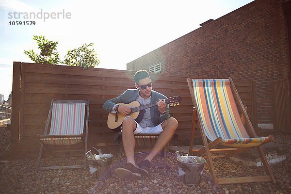 Mittlerer Erwachsener Mann spielt Gitarre auf dem Liegestuhl auf der Dachparty