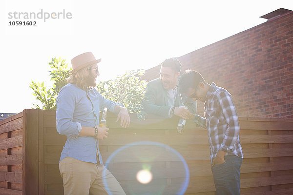 Drei männliche Freunde beim Plaudern und Biertrinken auf der Dachparty
