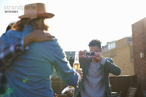 Junger Mann fotografiert männliche Freunde auf der Dachparty