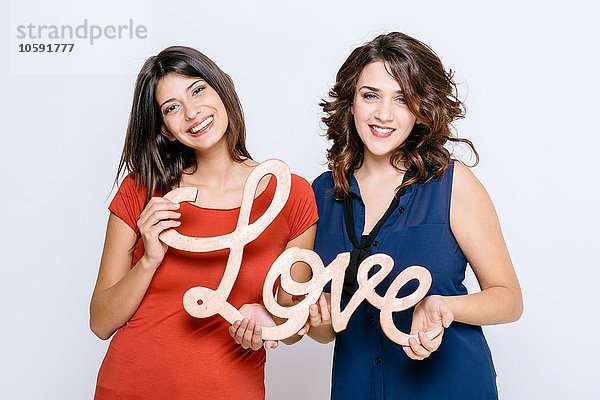 Lesbisches Paar  das das Wort Liebe hält  lächelnd in die Kamera blickend