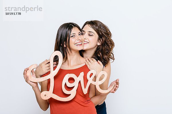 Lesbisches Paar  das das Wort Liebe hält  lächelnd in die Kamera blickend