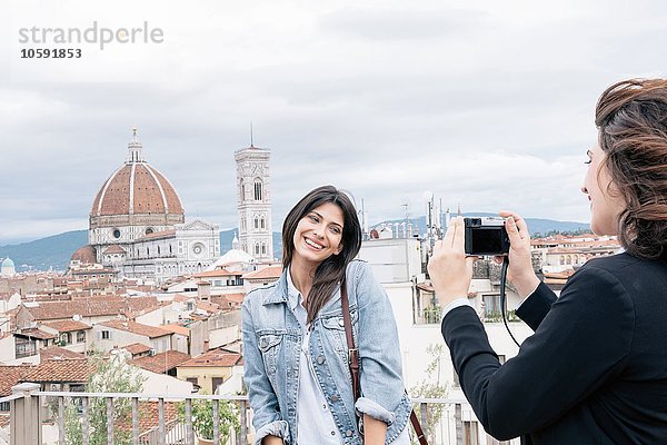 Junge Frau  die für einen Freund posiert und vor der Kathedrale von Florenz und dem Campanile von Giotto fotografiert  lächelnd über die Schulter schaut  Florenz  Toskana  Italien