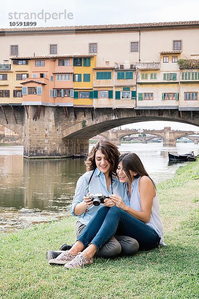 Lesbenpaar sitzt zusammen und schaut auf die Digitalkamera vor Ponte Vecchio lächelnd  Florenz  Toskana  Italien