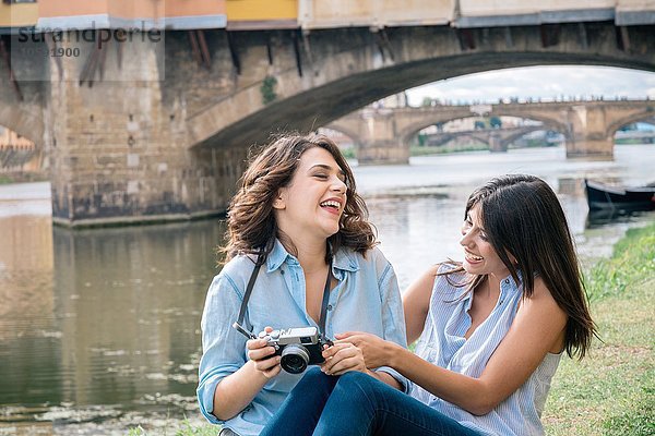 Lesbisches Paar sitzt zusammen und schaut lachend auf die Digitalkamera  vor Ponte Vecchio  Florenz  Toskana  Italien