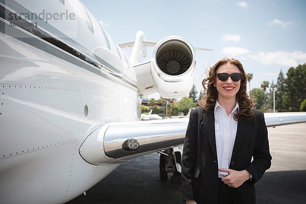 Portrait der mittleren erwachsenen Geschäftsfrau und des Privatjets am Flughafen