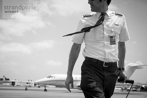 Schwarz-Weiß-Bild eines männlichen Privatjet-Piloten  der am Flughafen ankommt.