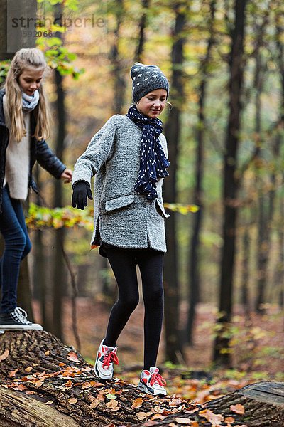 Mädchen auf Baumstamm im Herbstwald unterwegs