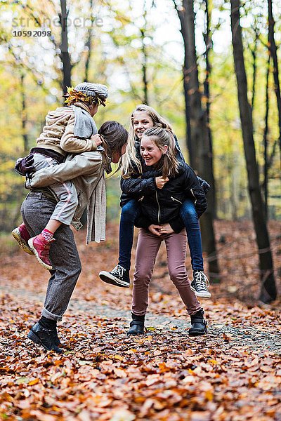 Mutter und Töchter beim Huckepackreiten im Herbstwald
