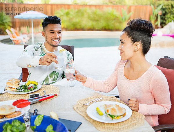 Junges Paar  das sich zum Essen im Freien hinsetzt und einen Toast ausspricht.