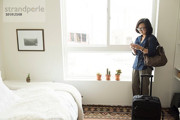 Reife Frau im Hotelzimmer mit Koffer und Smartphone