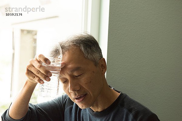 Reifer Mann hält Wasserflasche an den Stirnaugen geschlossen