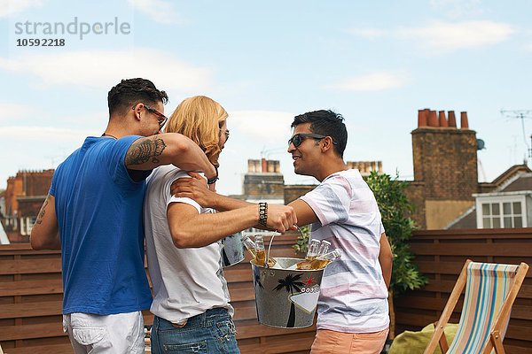Drei männliche Freunde tragen einen Eiskübel mit Flaschenbier auf der Dachparty.