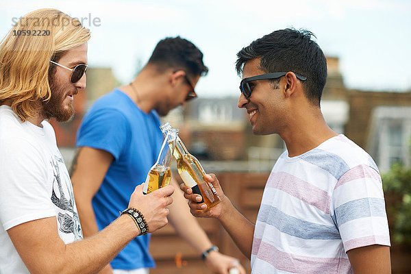Zwei männliche Freunde stoßen mit Flaschenbier auf der Dachparty an.