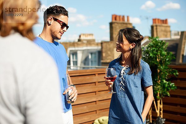 Männliche und weibliche Freunde beim Plaudern und Trinken auf der Dachparty