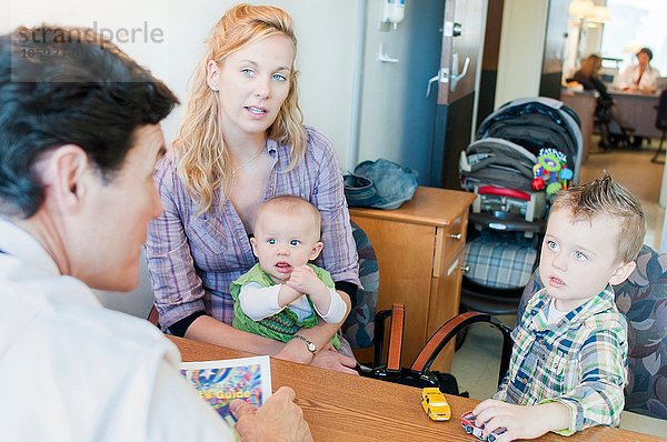 Mutter sitzend mit zwei Kindern  im Gespräch mit dem Arzt