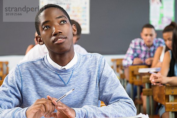 Porträt eines männlichen Schülers  sitzend am Schreibtisch im Klassenzimmer