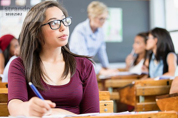 Studentin  sitzt am Schreibtisch im Klassenzimmer  schreibt