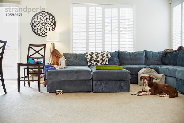 Mädchen mit digitalem Tablett auf Sofa im Wohnzimmer  Hund hinter ihr