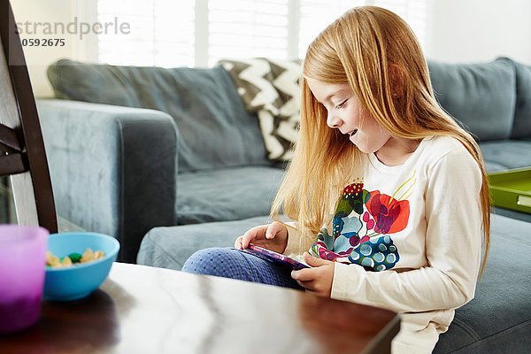 Mädchen mit digitalem Tablett auf Sofa im Wohnzimmer