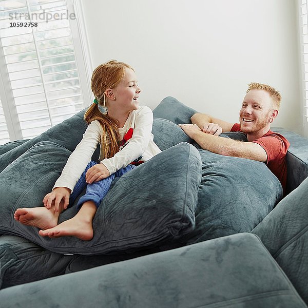 Vater und Tochter spielen auf Kissenstapel im Wohnzimmer