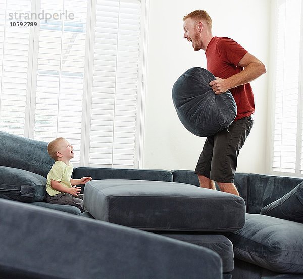 Vater mit Kissen spielt mit Sohn im Wohnzimmer