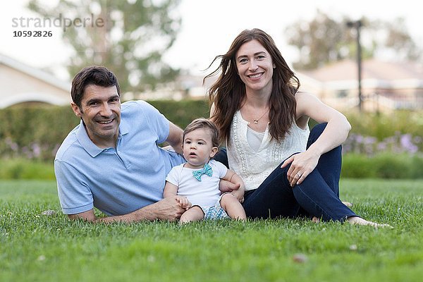 Familie mit Baby auf Gras sitzend und lächelnd in die Kamera schauend