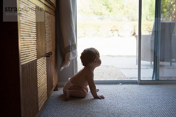 Seitenansicht des Babys  das vor Terrassentüren sitzt und wegschaut.