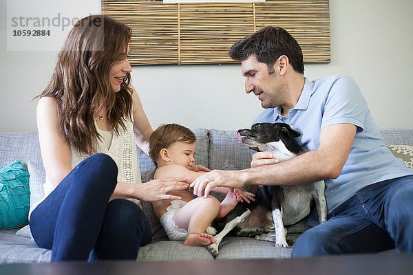 Familie mit Babyjunge auf Sofa sitzend  mit Hund spielend