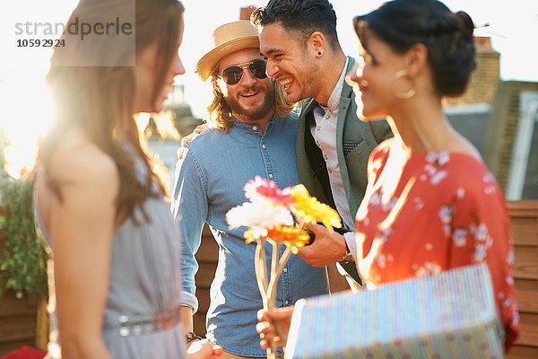 Freunde bei der Party auf der Dachterrasse mit Blumen und einem Lächeln als Geschenk