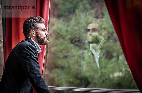 Seitenansicht eines erwachsenen Mannes im Anzug mit Blick aus dem Fenster