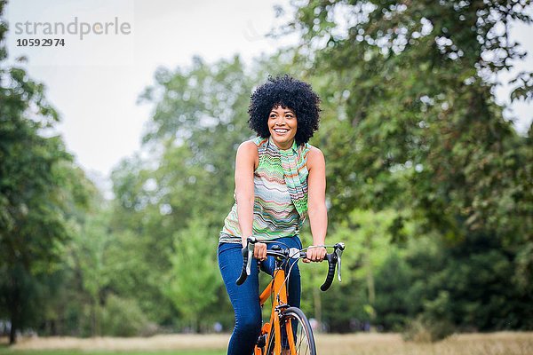 Vorderansicht einer reifen Frau mit einem Afro-Fahrrad  die lächelnd davonschaut.